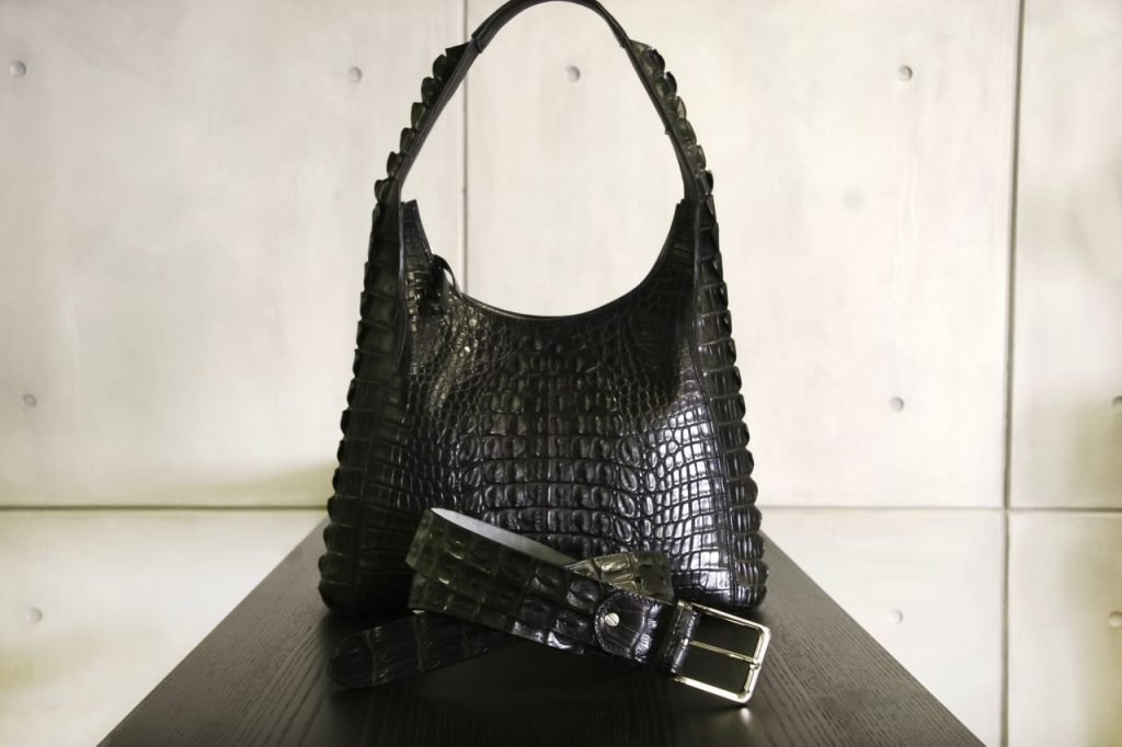 Elegant black crocodile leather handbag paired with a matching belt on a sleek surface.